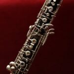 Detailed close-up of an oboe with intricate keys set against a rich red background, highlighting its elegance.