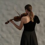 Professional female violinist in a black dress captivatingly plays indoors, focusing on her craft.