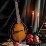 Romantic still life featuring a mandolin, apples, candles, and classic drapery.